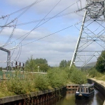 Heyrod, UK: Huddersfield Narrow Canal passes under a pylon. A substation was built while the canal was closed to navigation, and when it was reopened had to pass between the pylon's legs. [Picture by Peter Freeman]